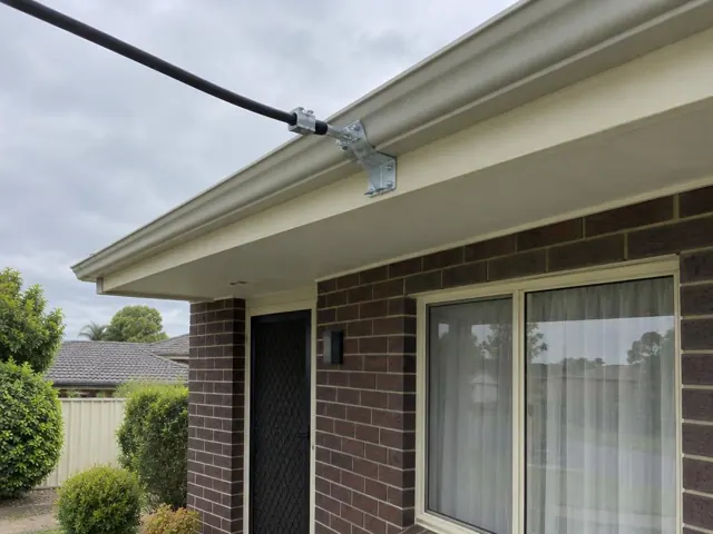 Overhead service cable fixed to a house eave with a metal point-of-attachment bracket on brick veneer in Speers Point