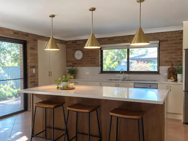 Three brass pendant lights over a kitchen island in a brick-walled home with tiled floors in Booragul