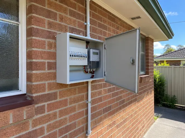 Open external switchboard on a brick house wall beside a window in Boolaroo